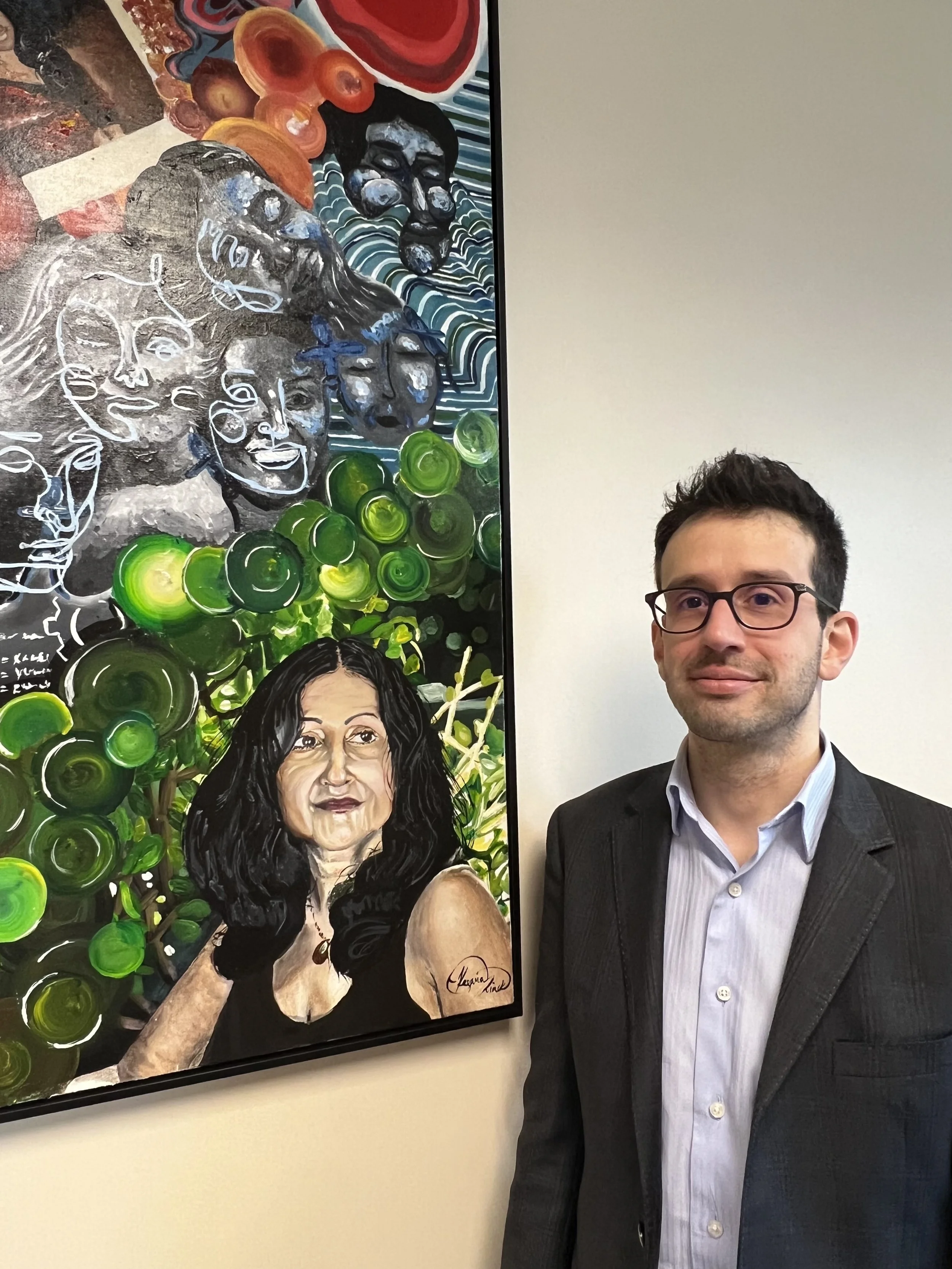  AU Spanish professor Christopher Botero poses next to a painting of critically acclaimed Puerto Rican author Judith Ortiz Cofer in the main suite of the EWL office.  (photo courtesy of Keyvia Mack)  