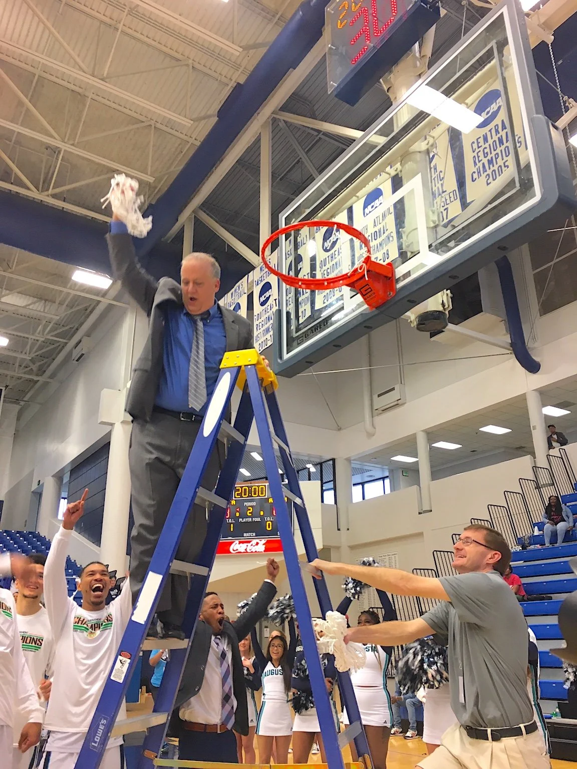  AU coach Dip Metress cuts down the nets after his Jaguars won the 2019 Peach Belt Conference Tournament at Christenberry Fieldhouse. At the top of the page, Metress now has 600 career wins in 30 seasons—22 at AU and eight seasons at Belmont Abbey. (Bell Ringer file photos) 