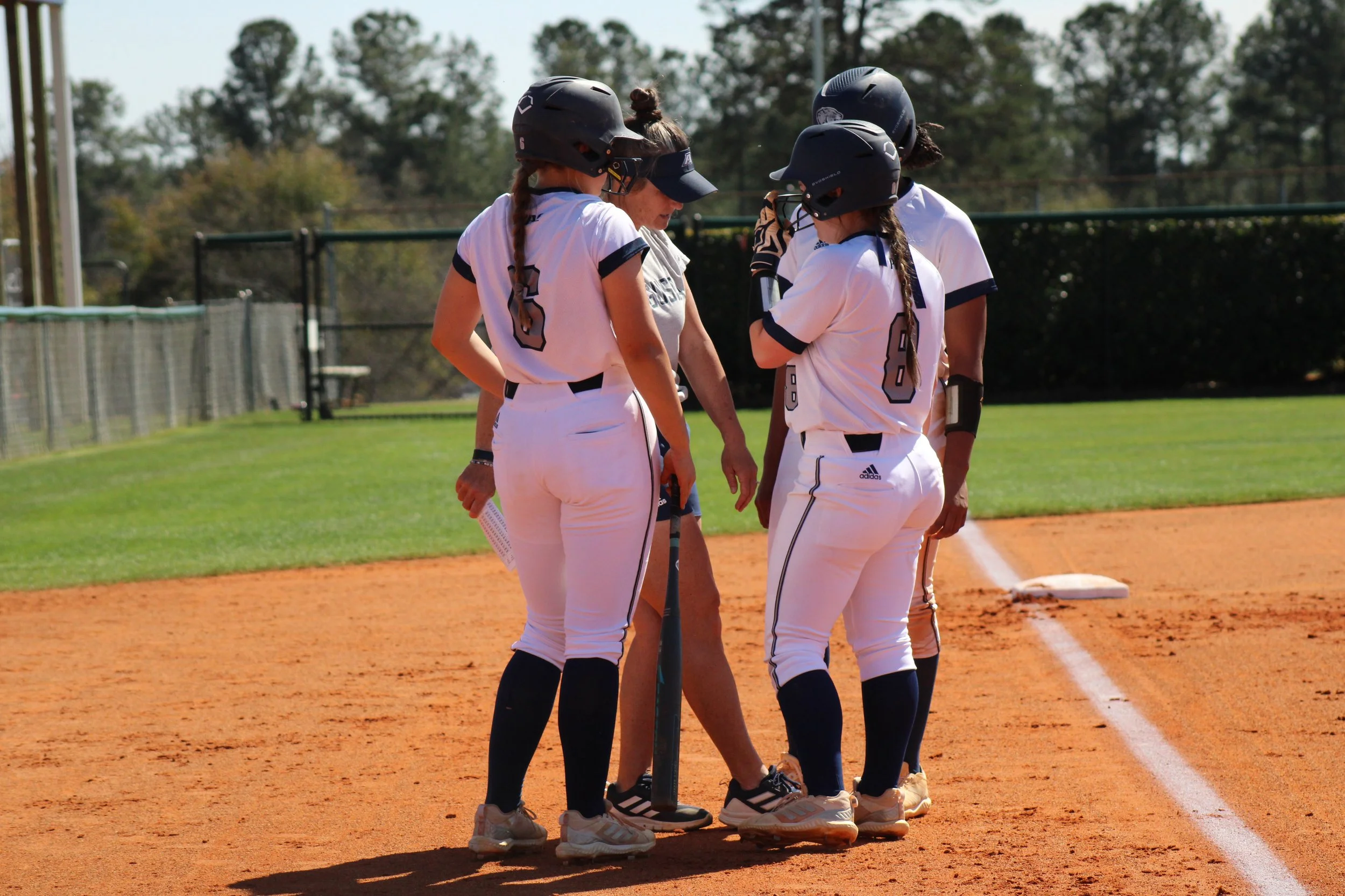  AU softball coach Melissa Brocato, Paige Patterson (6) and Olivia Biles (8), along with Jakayla Sullivan (behind Biles), huddle during a break in the action. At the top of the page, Trevor Maddox bats for the AU baseball team, which lost all three games at home against Young Harris. Maddox hit three hits in the series, including a double. (photos by Chris Rickerson)     